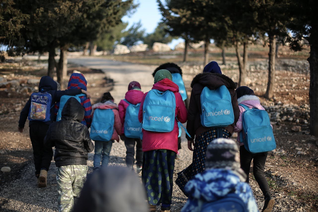 A group of children with UNICEF backpacks walking on a dirt road in rural Syria.