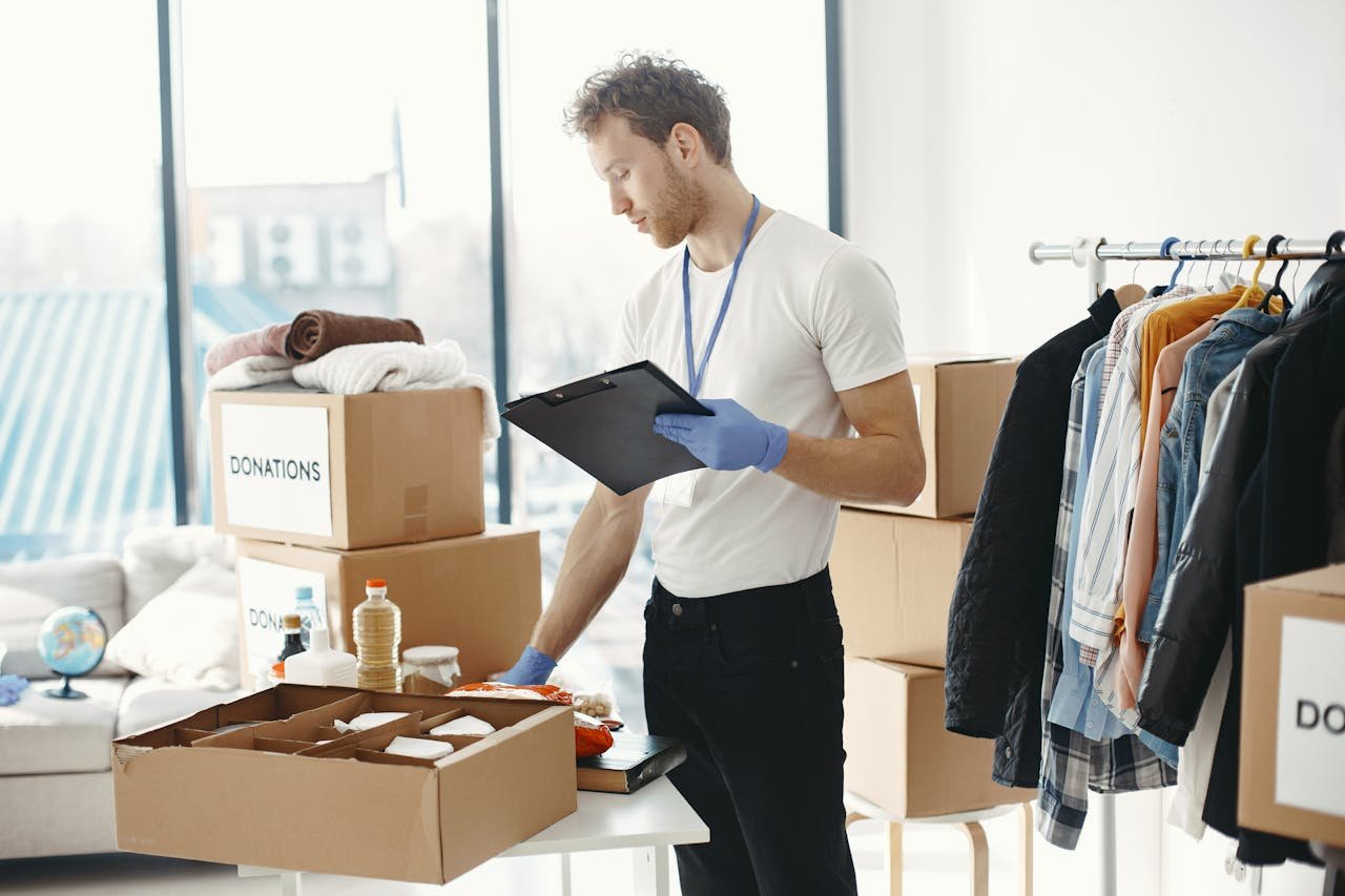 A volunteer organizes charitable donations and clothing indoors with a clipboard.
