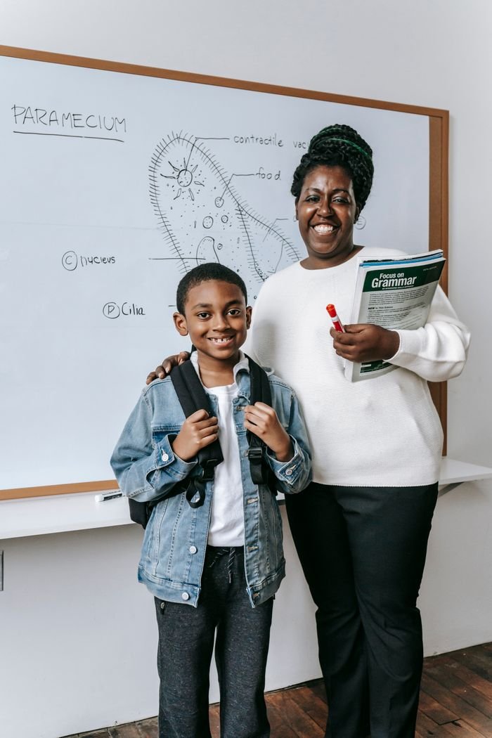 Cheerful teacher holding books and embracing African American little boy while looking at camera